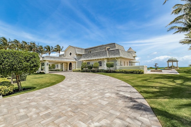 477 S Beach Rd, Jupiter Island, FL 33455 - view of front facade featuring a front yard, curved driveway, mansard roof, a balcony, and a shingled roof