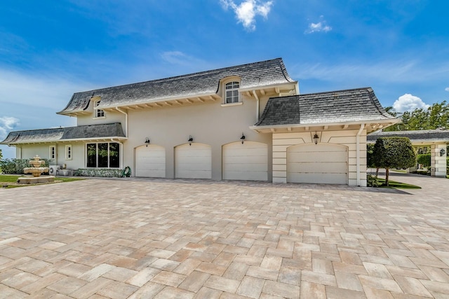 477 S Beach Rd, Jupiter Island, FL 33455 - view of front facade featuring a garage, decorative driveway, mansard roof, a high end roof, and stucco siding