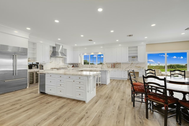 kitchen with a center island, white cabinets, wall chimney range hood, light wood-type flooring, and appliances with stainless steel finishes