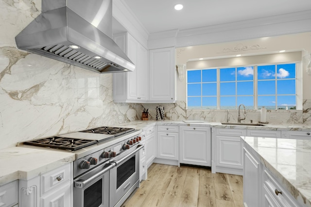 kitchen with range with two ovens, wall chimney range hood, sink, light wood-type flooring, and white cabinetry