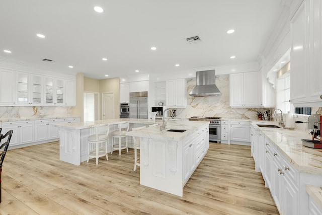 kitchen featuring a large island, sink, white cabinets, and wall chimney range hood