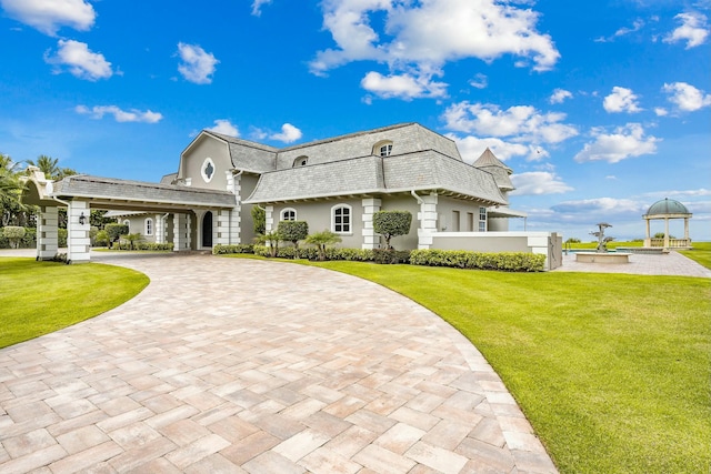 477 S Beach Rd, Jupiter Island, FL 33455 - view of front property with a front yard, mansard roof, decorative driveway, stucco siding, and a shingled roof