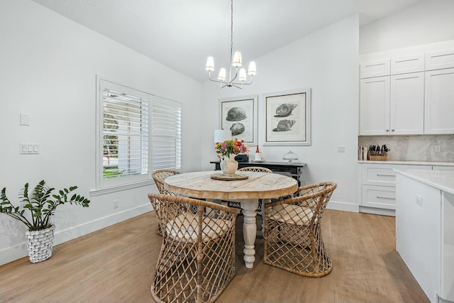 dining area with light wood-type flooring, lofted ceiling, and an inviting chandelier