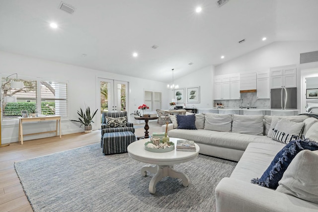 living room featuring a notable chandelier, lofted ceiling, french doors, and light hardwood / wood-style flooring