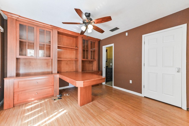 unfurnished office featuring built in desk, ceiling fan, and light hardwood / wood-style flooring