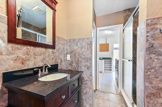 bathroom with a shower with door, tile walls, tile patterned floors, and vanity