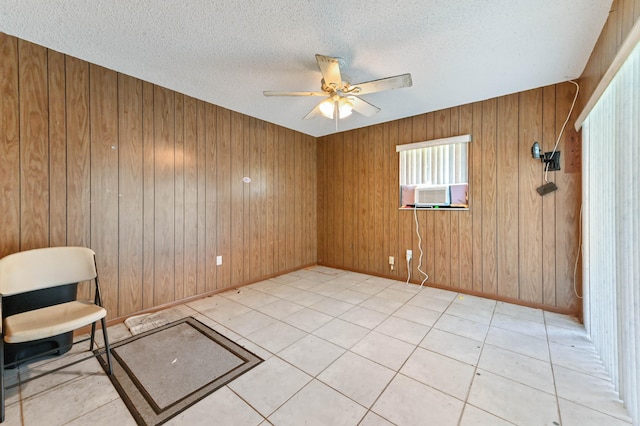 unfurnished room featuring ceiling fan, light tile patterned floors, a textured ceiling, wood walls, and cooling unit