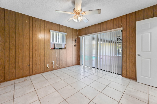 tiled empty room featuring ceiling fan, a textured ceiling, cooling unit, and wooden walls