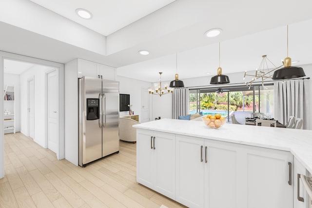 kitchen featuring stainless steel fridge, decorative light fixtures, white cabinetry, light stone countertops, and an inviting chandelier