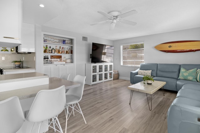 living room with bar, light hardwood / wood-style floors, and ceiling fan