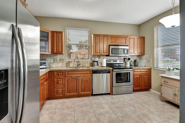 kitchen with hanging light fixtures, sink, stainless steel appliances, and a wealth of natural light