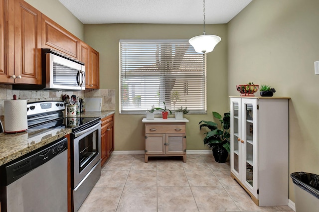 kitchen with backsplash, hanging light fixtures, light tile patterned floors, light stone counters, and stainless steel appliances