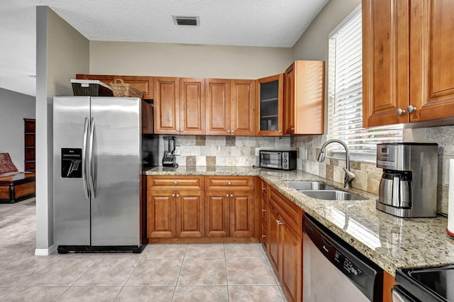 kitchen featuring a textured ceiling, stainless steel appliances, light stone counters, and sink