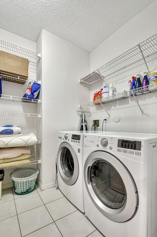 laundry area featuring washing machine and clothes dryer, a textured ceiling, and light tile patterned flooring