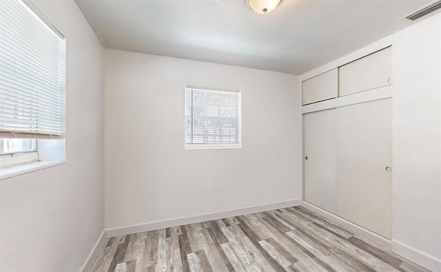 unfurnished bedroom featuring multiple windows, a closet, and light wood-type flooring