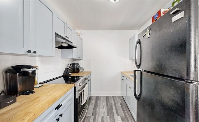 kitchen featuring wood counters, black fridge, stainless steel range with electric cooktop, white cabinets, and light wood-type flooring