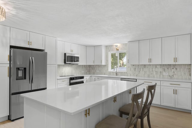 kitchen with sink, appliances with stainless steel finishes, backsplash, white cabinets, and a kitchen island