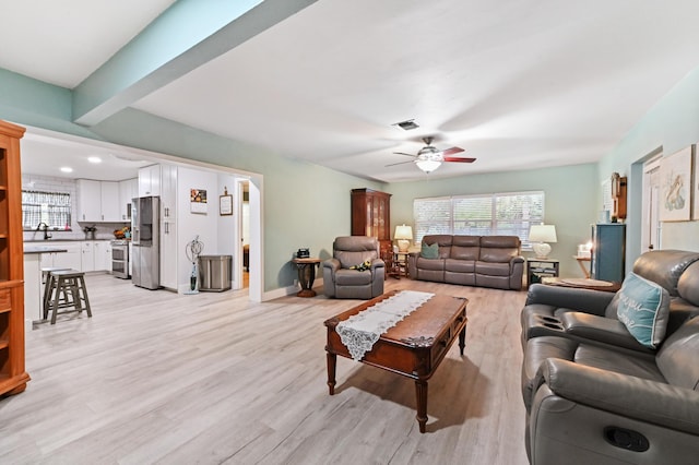 living room featuring sink, beam ceiling, light hardwood / wood-style floors, and ceiling fan