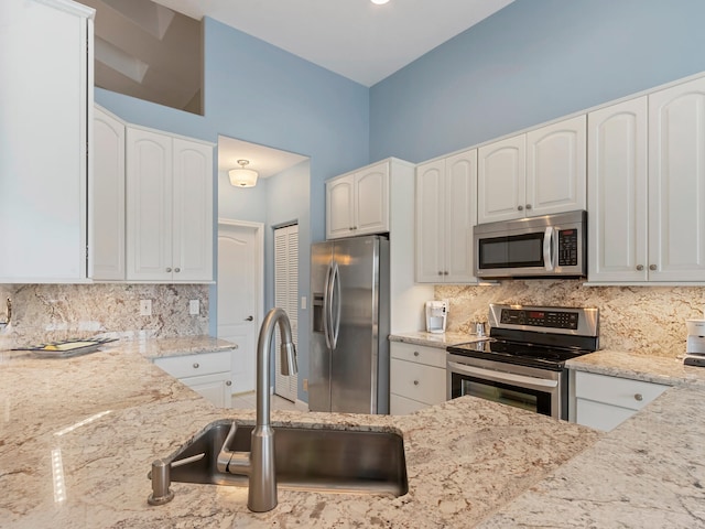 kitchen featuring light stone countertops, appliances with stainless steel finishes, tasteful backsplash, sink, and white cabinets