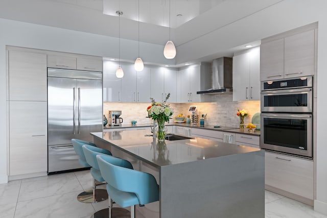 kitchen with backsplash, wall chimney exhaust hood, a breakfast bar, stainless steel appliances, and pendant lighting