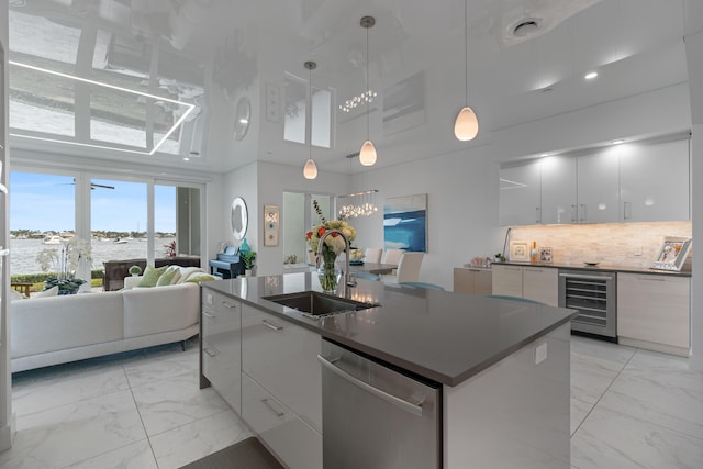 kitchen featuring a towering ceiling, stainless steel dishwasher, beverage cooler, sink, and white cabinets