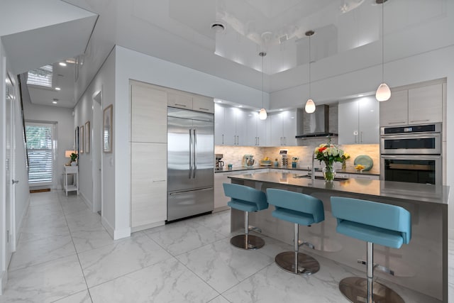 kitchen with a towering ceiling, backsplash, wall chimney exhaust hood, stainless steel appliances, and hanging light fixtures