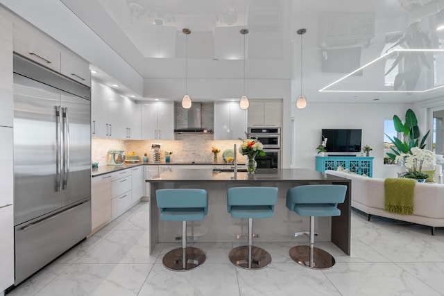 kitchen with a towering ceiling, appliances with stainless steel finishes, pendant lighting, and wall chimney exhaust hood