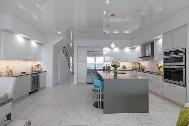 kitchen featuring a center island, wall chimney range hood, hanging light fixtures, a towering ceiling, and appliances with stainless steel finishes