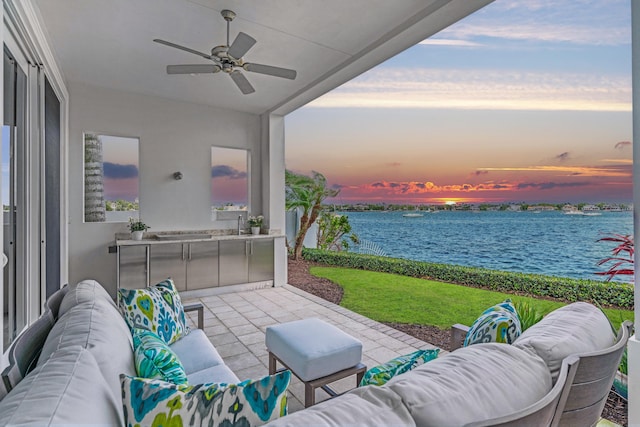 patio terrace at dusk featuring a water view and ceiling fan