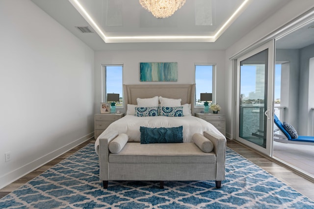 bedroom with access to outside, a raised ceiling, dark hardwood / wood-style flooring, and a chandelier