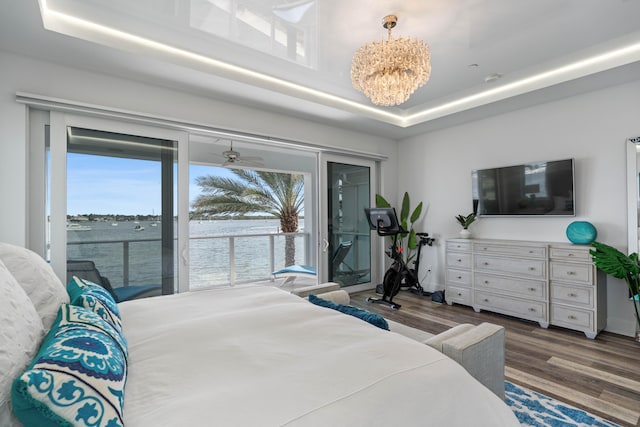 bedroom with access to exterior, a tray ceiling, a water view, a chandelier, and dark hardwood / wood-style floors