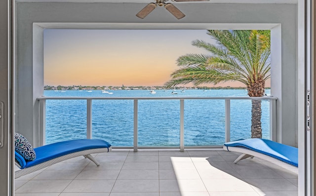 balcony at dusk with a water view and ceiling fan