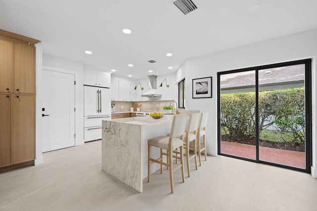 kitchen featuring a breakfast bar, white cabinets, wall chimney range hood, tasteful backsplash, and high end fridge