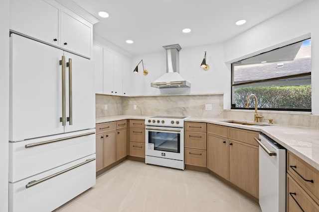 kitchen with decorative backsplash, white appliances, sink, wall chimney range hood, and white cabinetry