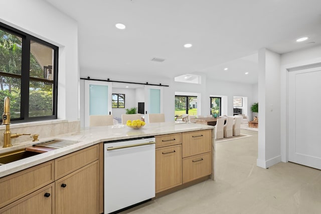 kitchen featuring white dishwasher, sink, a barn door, light brown cabinetry, and a healthy amount of sunlight