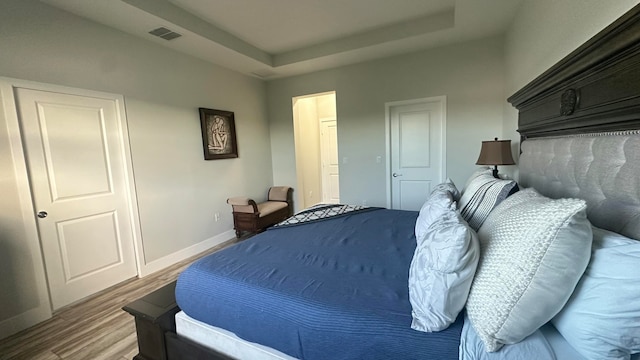 bedroom with wood-type flooring and a tray ceiling