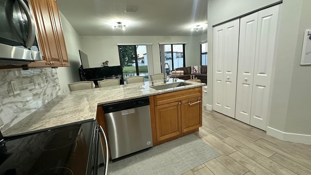 kitchen featuring backsplash, sink, light stone countertops, appliances with stainless steel finishes, and light hardwood / wood-style floors