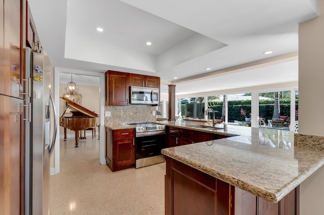 kitchen with sink, stainless steel appliances, light stone counters, kitchen peninsula, and a tray ceiling