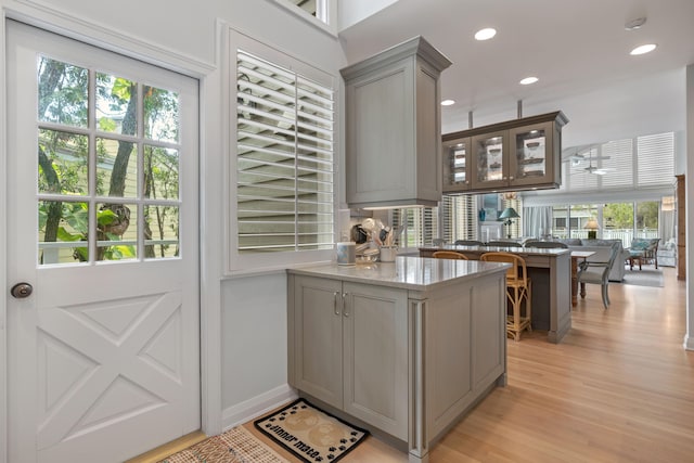 bar with gray cabinetry, ceiling fan, light hardwood / wood-style flooring, and light stone counters