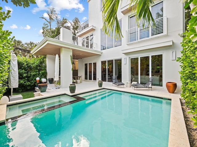 rear view of property featuring a balcony, a pool with hot tub, and a patio area