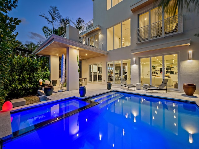 pool at dusk featuring an in ground hot tub and a patio area