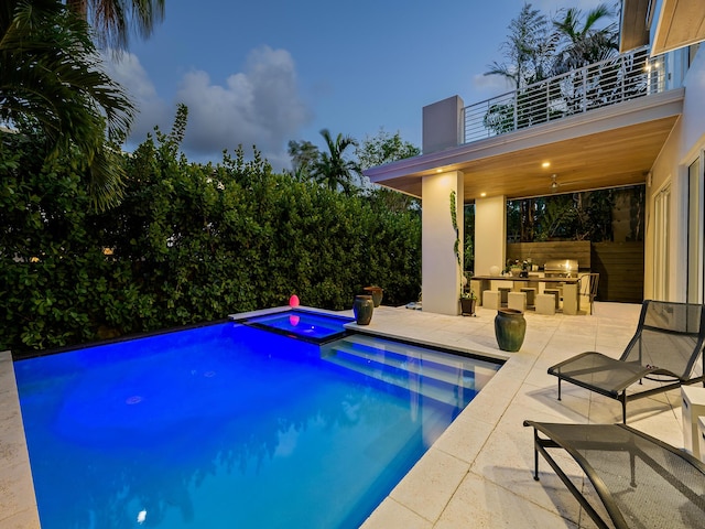 pool at dusk with a patio area, an outdoor kitchen, and an in ground hot tub