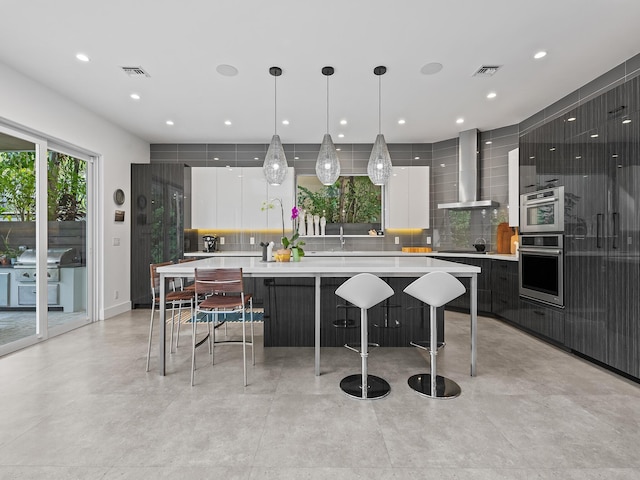 kitchen with wall chimney exhaust hood, decorative light fixtures, a large island, decorative backsplash, and white cabinets