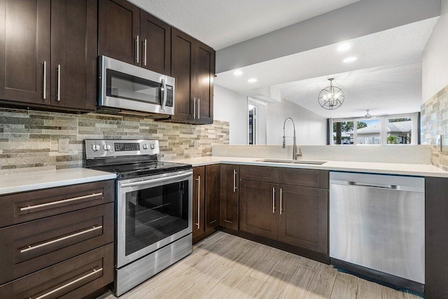 kitchen featuring sink, decorative backsplash, a textured ceiling, appliances with stainless steel finishes, and a notable chandelier