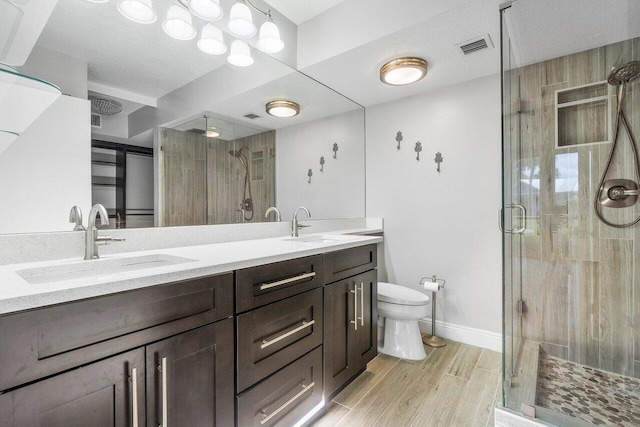 bathroom featuring vanity, wood-type flooring, toilet, a textured ceiling, and a shower with shower door