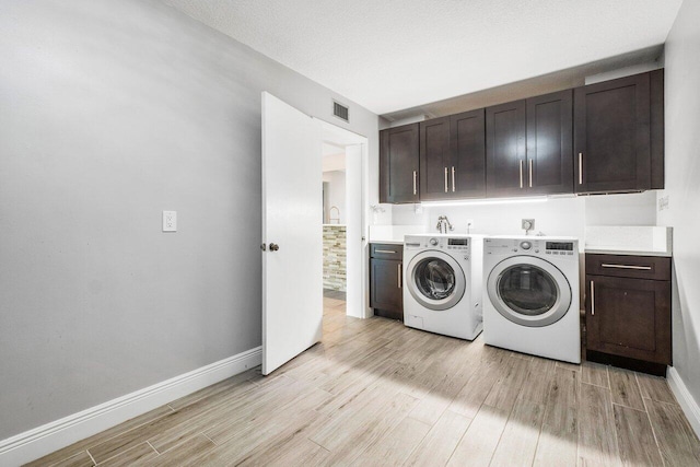 laundry area featuring a textured ceiling, cabinets, light hardwood / wood-style flooring, and washing machine and clothes dryer