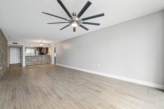 unfurnished living room with light hardwood / wood-style flooring, ceiling fan with notable chandelier, and a textured ceiling