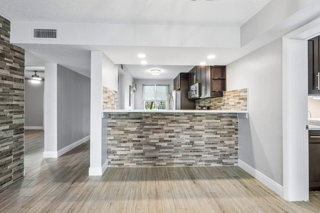 kitchen featuring wood-type flooring, dark brown cabinetry, a textured ceiling, kitchen peninsula, and stainless steel appliances