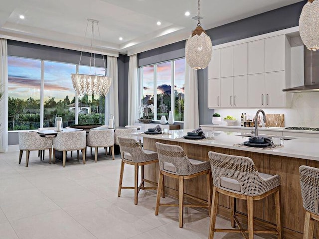 kitchen with a breakfast bar, a raised ceiling, white cabinets, a chandelier, and hanging light fixtures