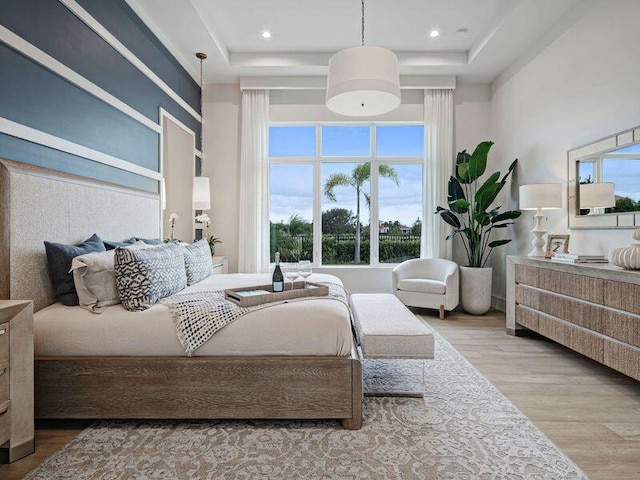 bedroom with a high ceiling, a tray ceiling, and light hardwood / wood-style flooring